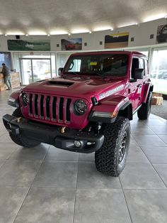 a red jeep parked in a showroom with people walking around the building behind it