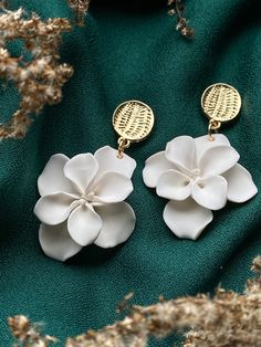 two white flower shaped earrings sitting on top of a green cloth