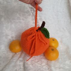 a hand is holding an orange knitted ornament next to some lemons