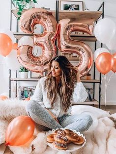 a woman sitting on the floor in front of balloons and some donuts with icing