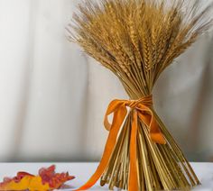 a bundle of dried wheat sitting on top of a table next to a fall leaf