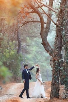 a bride and groom standing in the middle of a dirt road next to some trees