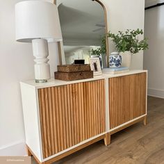 a white and wood dresser with a large mirror on it's sideboard next to a lamp