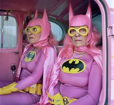 two women dressed as batman sit in the back of a pink van with yellow glasses