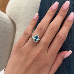 a woman's hand with a blue ring on her finger and the other hand holding an engagement ring