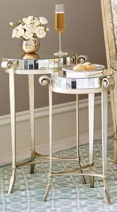 a glass table with flowers and a wine glass on it next to a mirror in a room