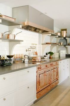 a large kitchen with white cabinets and copper accessories on the counter tops, along with an oven