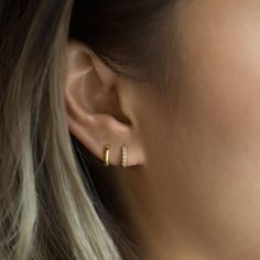 a close up of a person wearing a gold earring with two small diamonds on it