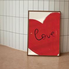 a red heart with the word love written on it in front of a white tiled wall