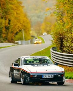 a white sports car driving down a road next to trees with yellow leaves on it