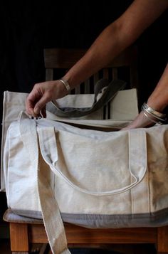 a person sitting on a chair with a white bag in their lap and one hand holding the strap