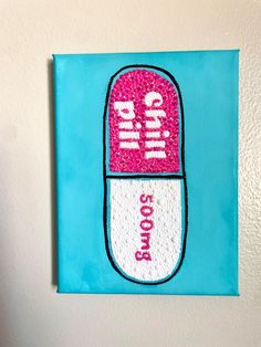 a blue and white wall hanging with a pink pill on it