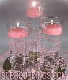 four candles are placed in glass vases with water and pink flowers on the table