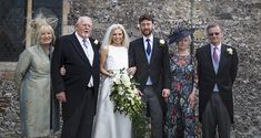 a group of people standing next to each other in front of a stone building with a bride and groom