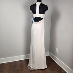 the back of a white dress on a mannequin stand in front of a wall