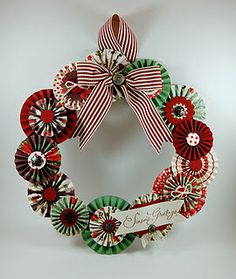 a christmas wreath with red, green and white paper flowers on the front is decorated with a ribbon