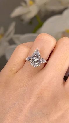 a woman's hand with a diamond ring on top of her finger and a flower in the background