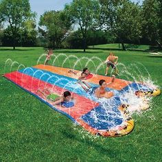 kids playing in an inflatable water slide on the grass with sprinkles