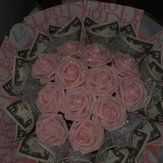 a bunch of pink roses sitting on top of a pile of dollar bills in a paper plate