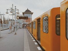 a yellow train parked next to a loading platform at a train station on a cloudy day