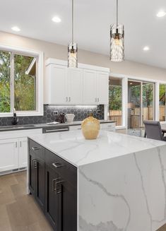 a large kitchen with marble counter tops and white cabinets, along with an island in the middle