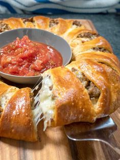 a meatball roll on a cutting board with a bowl of tomato sauce in the middle