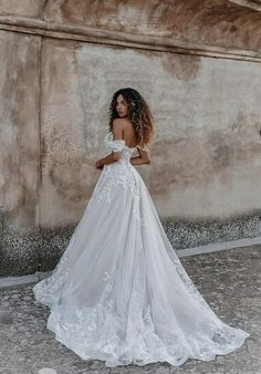 a woman in a white wedding dress standing against a stone wall with her back to the camera