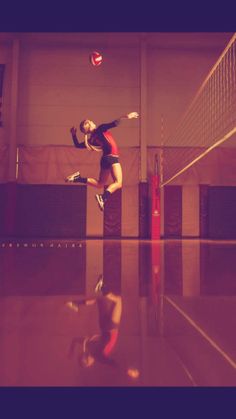 a woman jumping up to hit a ball with her racket in an indoor volleyball court