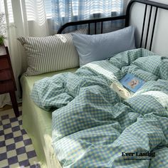 an unmade bed with blue and white checkered sheets, pillows and a book on it