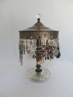 a lamp that is on top of a glass base with beads and chains hanging from it