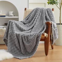 a chair with a blanket on top of it in front of a white rug and potted plant