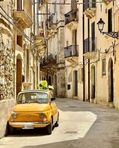 an old yellow car parked on the side of a road in front of tall buildings