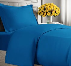 a bed with blue sheets and yellow flowers in a vase on the headboard next to it