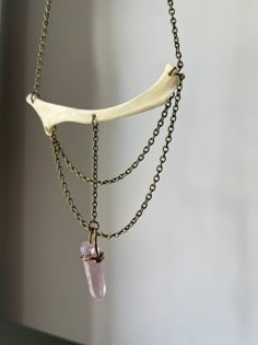 a piece of jewelry hanging from a chain with a pink stone on it's end