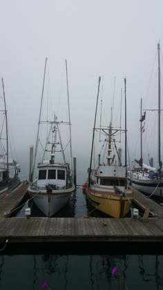 three boats docked at a dock in the ocean on a foggy, overcast day