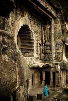 a woman standing in front of an ancient building with carvings on the walls and pillars