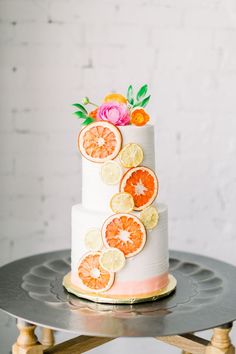 a white cake with oranges and flowers on top is sitting on a metal stand