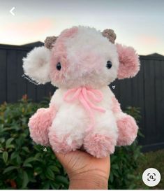 a hand holding a pink and white stuffed animal