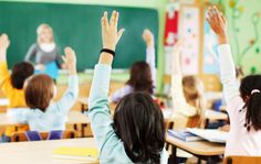 several children raising their hands in a classroom