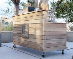 a large wooden box sitting on top of a cement floor next to a tree and fence