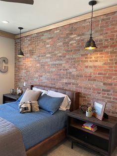 a bedroom with a brick wall behind the bed and two lamps hanging from the ceiling