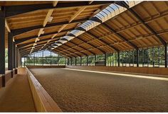 the inside of a building with lots of wood and glass on the roof, along with an enclosed area for horses to graze