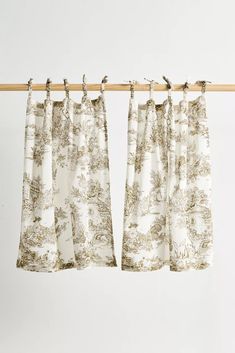 two curtains hanging on a wooden rod with white and brown print, in front of a white wall