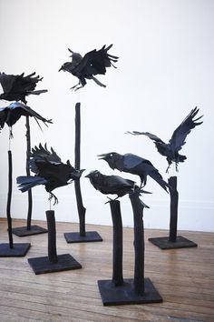 several black birds sitting on top of wooden posts in the middle of a wood floor