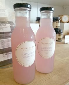 two bottles of lavender lemonade sit on a counter top in front of jars with labels