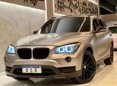 the front end of a silver bmw suv in a showroom with other cars behind it