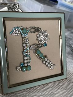 the letter k is made up of beads and other items in a frame on a bed