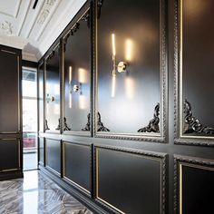 an elegantly decorated hallway with black walls and gold trimming on the wall, along with two sconces