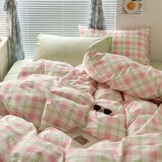 an unmade bed with pink and green checkered comforter, pillows and eyeglasses on it