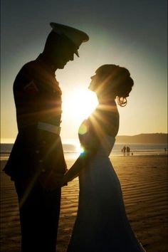 a man and woman standing on top of a beach next to the ocean at sunset